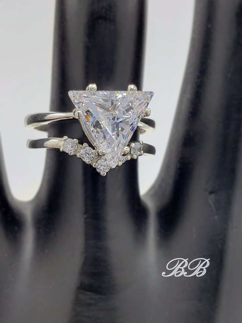 May include: A silver ring set with a large triangular-shaped clear stone and smaller clear stones on the band.