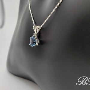 May include: A silver chain necklace with a pendant featuring a blue oval gemstone surrounded by smaller clear gemstones.