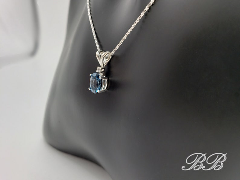 May include: A silver chain necklace with a pendant featuring a blue oval gemstone surrounded by smaller clear gemstones.