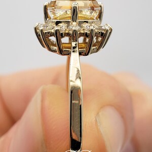 Pode incluir: Um anel de ouro com uma grande gema de top&aacute;zio amarelo redonda cercada por um halo de pequenos diamantes brancos redondos.