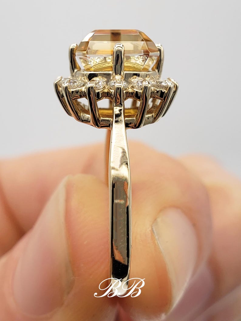 Pode incluir: Um anel de ouro com uma grande gema de top&aacute;zio amarelo redonda cercada por um halo de pequenos diamantes brancos redondos.