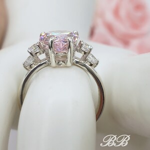 Puede incluir: Un anillo de plata con una gran piedra preciosa rosa de forma ovalada rodeada de piedras preciosas m&aacute;s peque&ntilde;as y transparentes.