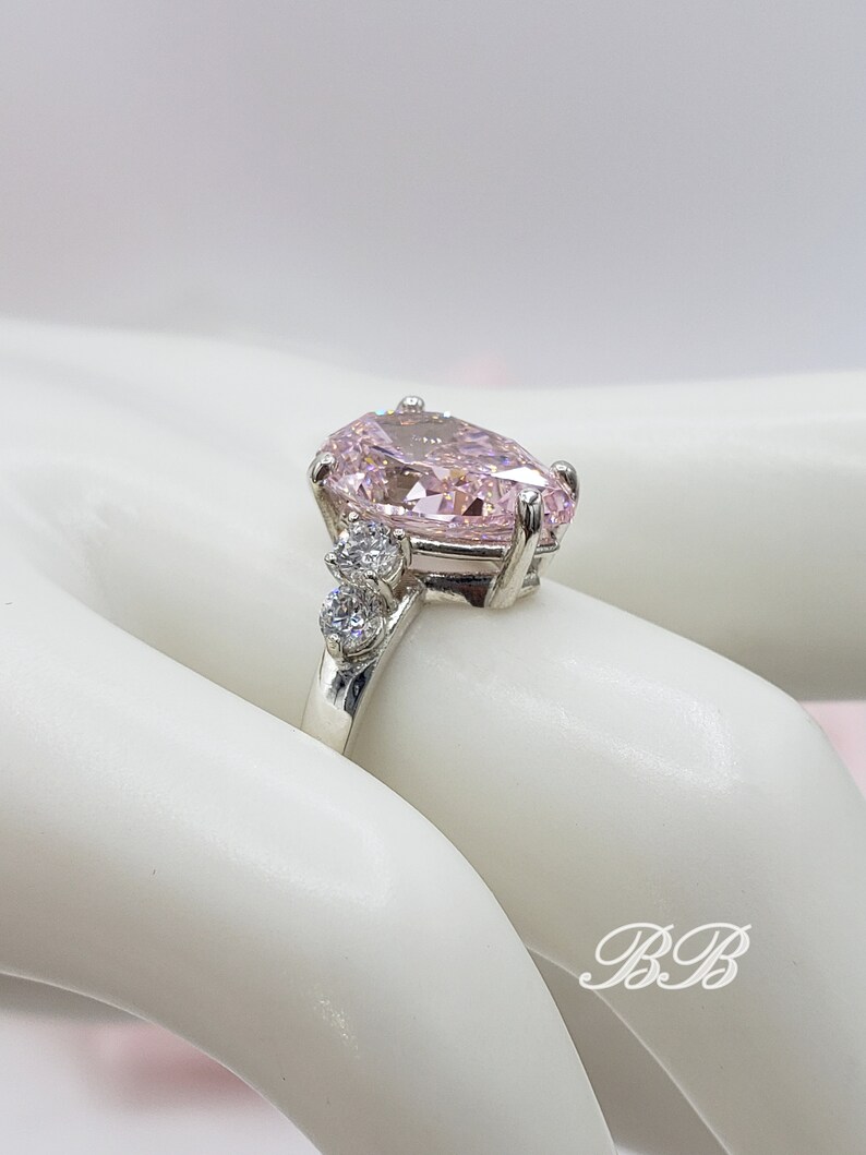 Puede incluir: Un anillo de plata con una gran piedra rosa en forma de pera y piedras redondas transparentes m&aacute;s peque&ntilde;as en la banda.