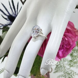 May include: A silver ring with a large, clear oval-shaped gemstone. The ring is on a mannequin hand.
