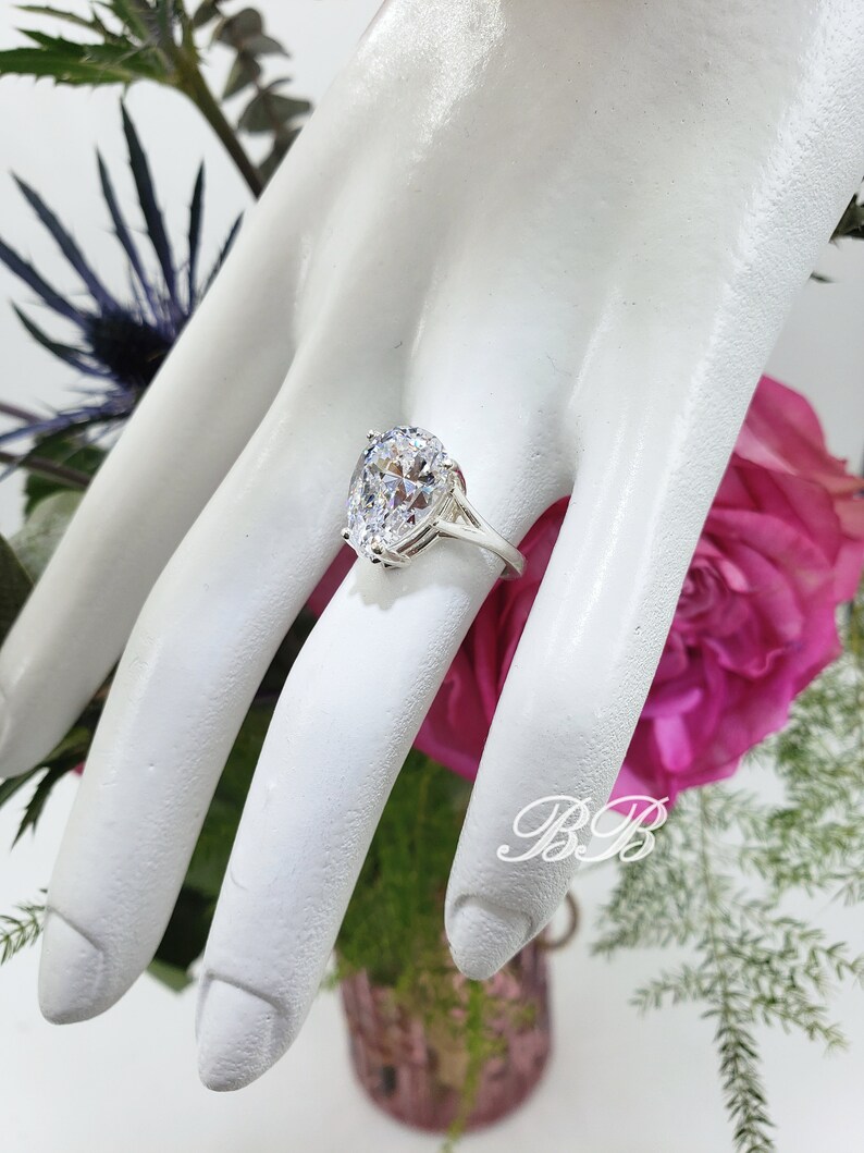 May include: A silver ring with a large, clear oval-shaped gemstone. The ring is on a mannequin hand.