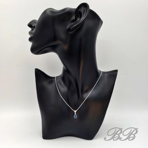 May include: A silver chain necklace with a blue gemstone pendant. The necklace is displayed on a black mannequin bust.