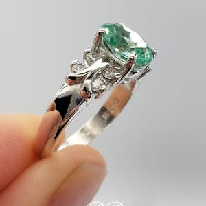 Puede incluir: Un anillo de plata con una piedra ovalada verde y piedras m&aacute;s peque&ntilde;as transparentes engastadas en un dise&ntilde;o de mariposa.