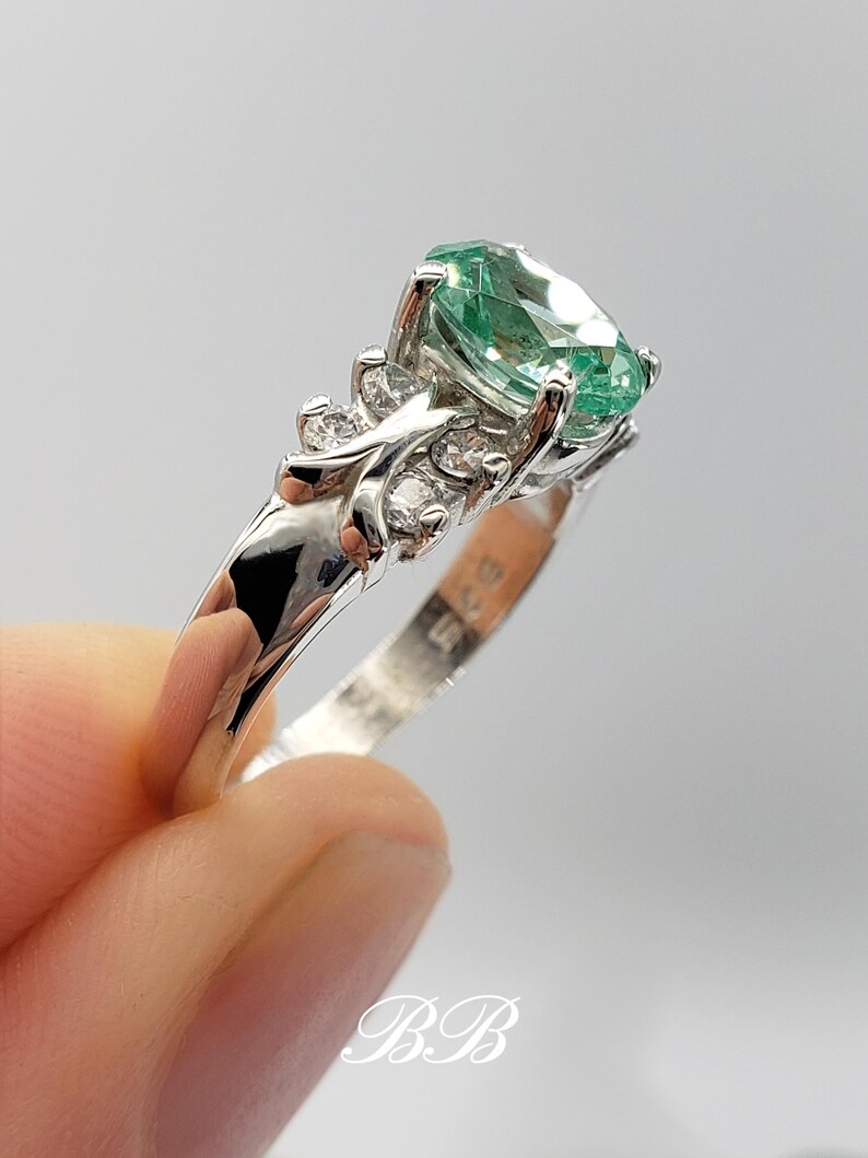 Puede incluir: Un anillo de plata con una piedra ovalada verde y piedras m&aacute;s peque&ntilde;as transparentes engastadas en un dise&ntilde;o de mariposa.