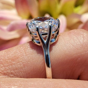 May include: A silver ring with a large, clear, round-cut gemstone set in a delicate, prong setting. The band is thin and has a simple design.