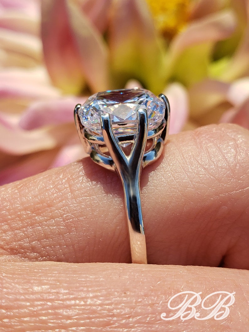 May include: A silver ring with a large, clear, round-cut gemstone set in a delicate, prong setting. The band is thin and has a simple design.