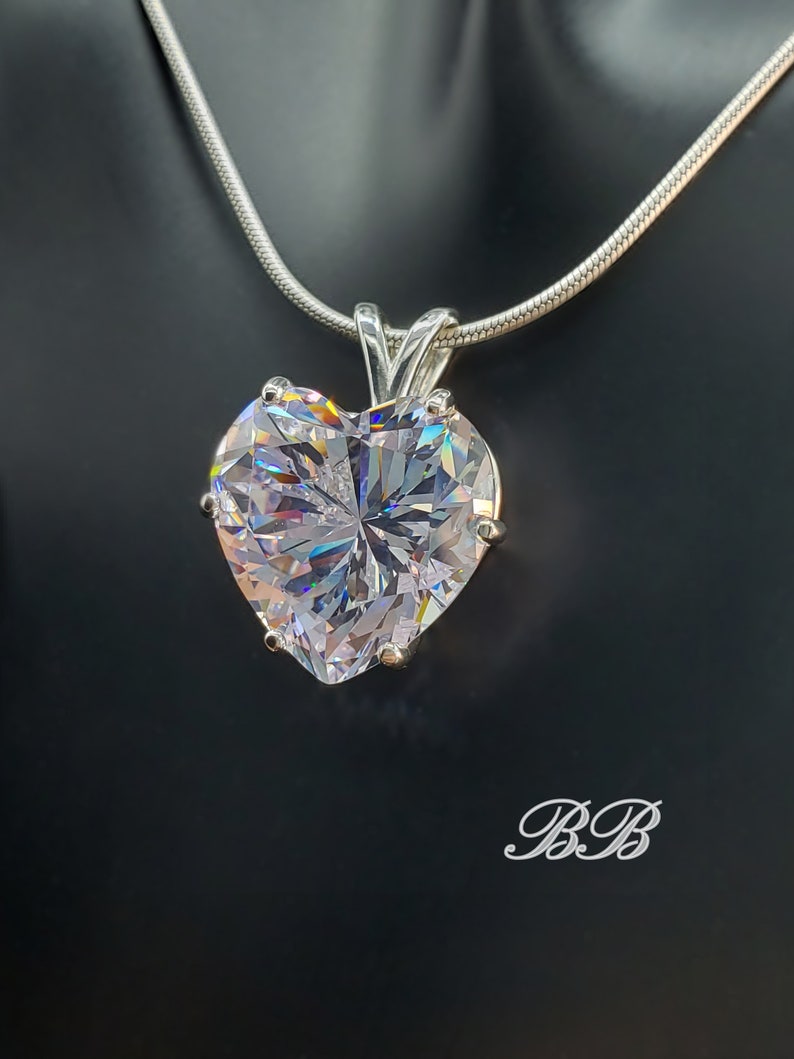 May include: A silver chain necklace with a large, clear heart-shaped pendant. The pendant is faceted and reflects light.