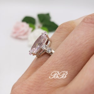 K&ouml;nnte beinhalten: Ein silberner Ring mit einem gro&szlig;en birnenf&ouml;rmigen rosafarbenen Edelstein und kleineren klaren Edelsteinen auf der Ringschiene.