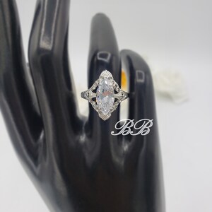 Puede incluir: Un anillo de plata con una piedra grande y transparente de forma marquesa engastada en un dise&ntilde;o de filigrana.