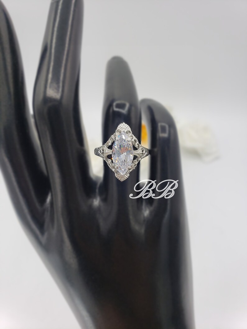 Puede incluir: Un anillo de plata con una piedra grande y transparente de forma marquesa engastada en un dise&ntilde;o de filigrana.