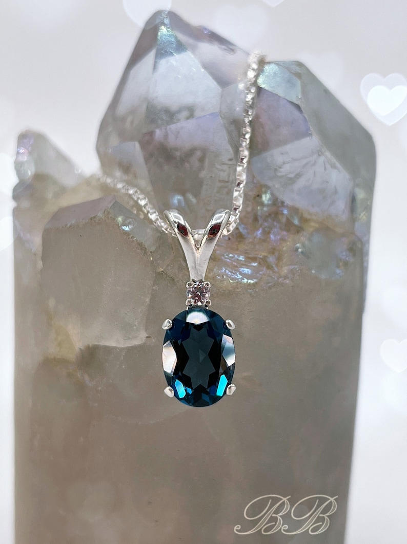 May include: A silver necklace with a dark blue oval pendant and a small diamond accent. The pendant is set in a silver bezel.