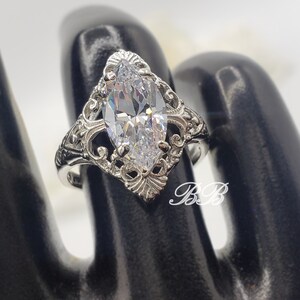 Puede incluir: Un anillo de plata con una piedra grande y transparente de forma marquesa engastada en un dise&ntilde;o de filigrana.