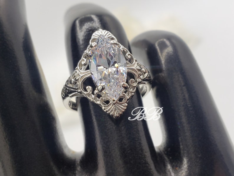Puede incluir: Un anillo de plata con una piedra grande y transparente de forma marquesa engastada en un dise&ntilde;o de filigrana.