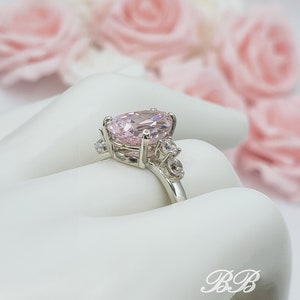 Puede incluir: Un anillo de plata con una gran piedra ovalada rosa rodeada de piedras peque&ntilde;as transparentes.