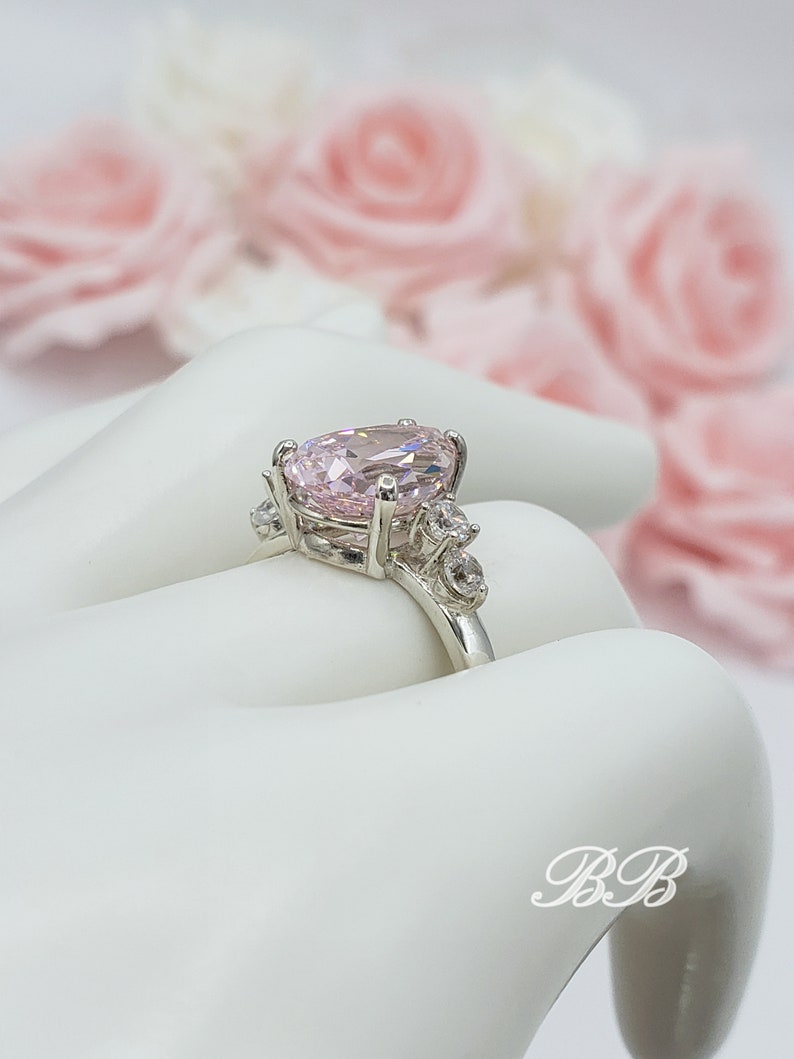 Puede incluir: Un anillo de plata con una gran piedra ovalada rosa rodeada de piedras peque&ntilde;as transparentes.