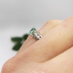 Puede incluir: Un anillo de plata con una piedra preciosa verde y detalles florales intrincados. El anillo est&aacute; en un dedo.