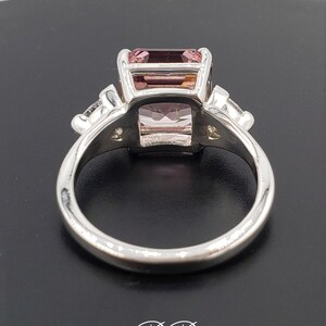 Puede incluir: Un anillo de plata con una gema rosa rectangular como elemento central. El anillo tiene gemas claras m&aacute;s peque&ntilde;as a ambos lados de la piedra principal. La banda pulida es lisa, con las iniciales "BB" en escritura en la base.