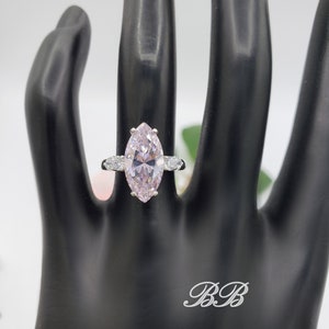 K&ouml;nnte beinhalten: Ein silberner Ring mit einem gro&szlig;en, birnenf&ouml;rmigen, hellrosa Edelstein, der von kleineren, klaren Edelsteinen umgeben ist.