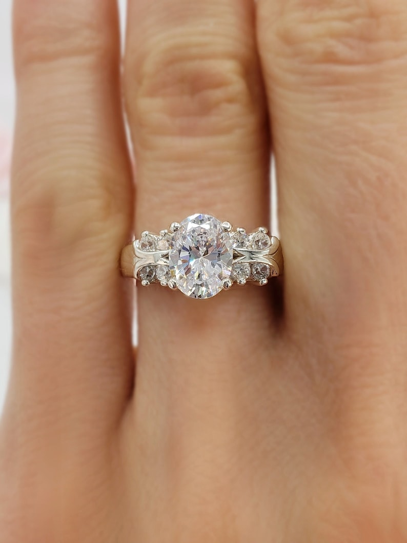 May include: A silver ring with an oval-shaped center stone and smaller stones set around it.