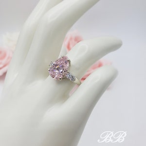 Puede incluir: Un anillo de plata con una gran piedra rosa en forma de pera rodeada de piedras peque&ntilde;as transparentes.