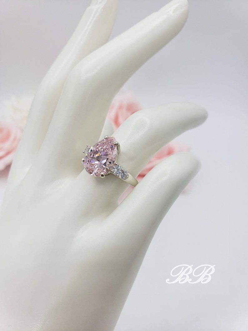 Puede incluir: Un anillo de plata con una gran piedra rosa en forma de pera rodeada de piedras peque&ntilde;as transparentes.