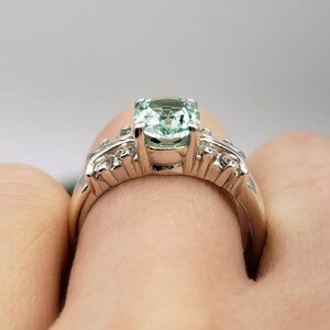 Puede incluir: Un anillo de plata con una piedra preciosa verde claro y piedras preciosas m&aacute;s peque&ntilde;as transparentes engastadas en una banda.
