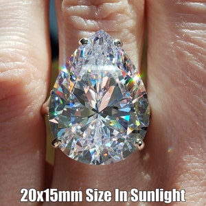May include: A pear-shaped clear crystal ring with a silver band. The ring is 20x15mm in size and is shown in sunlight.