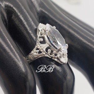 Puede incluir: Un anillo de plata con una piedra grande y transparente de forma marquesa engastada en un dise&ntilde;o de filigrana.