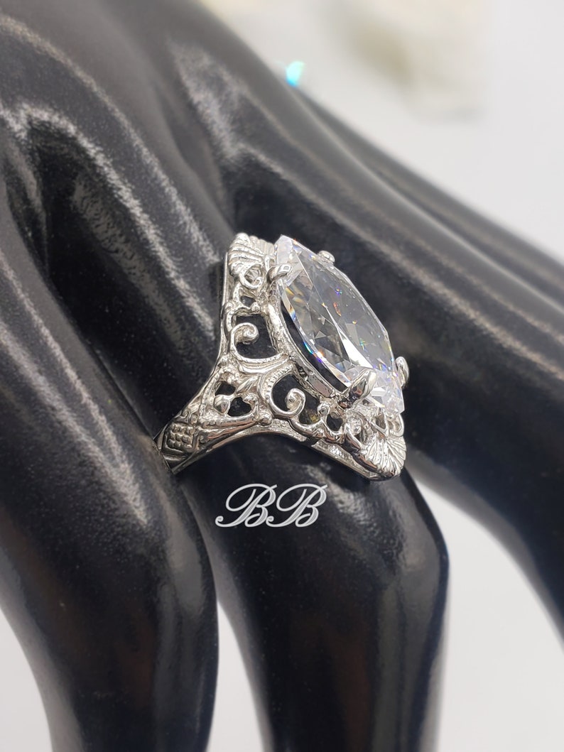 Puede incluir: Un anillo de plata con una piedra grande y transparente de forma marquesa engastada en un dise&ntilde;o de filigrana.