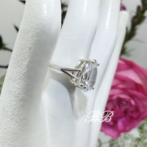 May include: A silver ring with a large, clear oval-shaped gemstone. The ring is set on a white mannequin hand.
