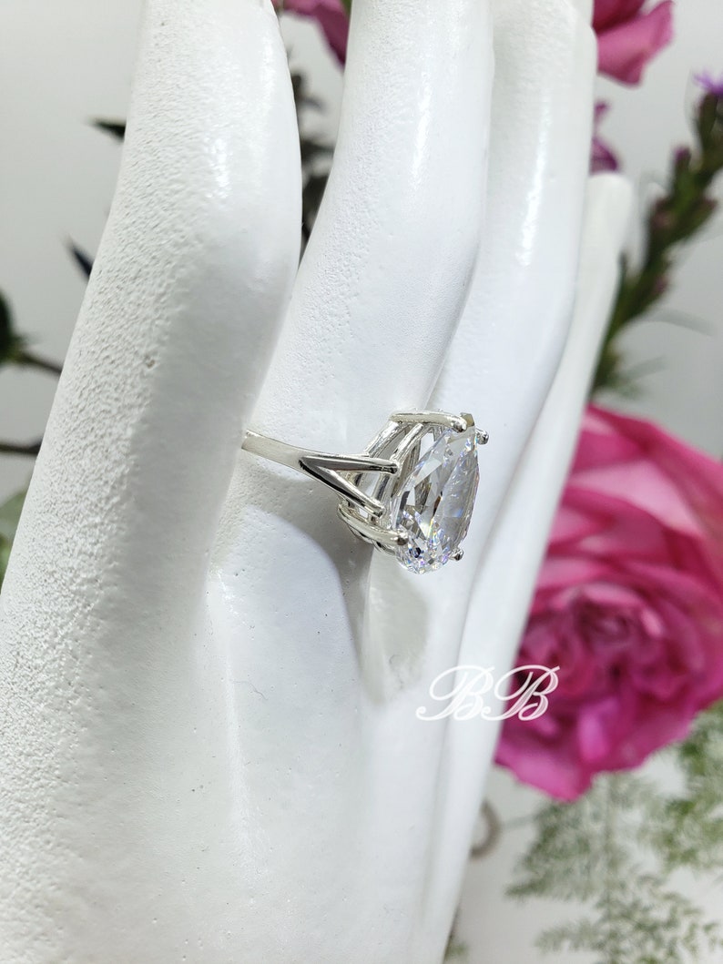May include: A silver ring with a large, clear oval-shaped gemstone. The ring is set on a white mannequin hand.