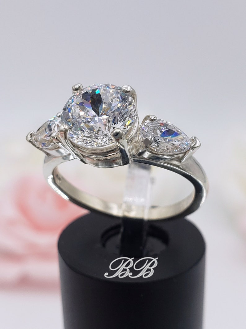 May include: A silver ring with three clear round and pear-shaped cubic zirconia stones.