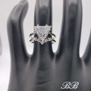 May include: A silver ring with a large triangular-shaped clear stone and a smaller band of stones around the base.