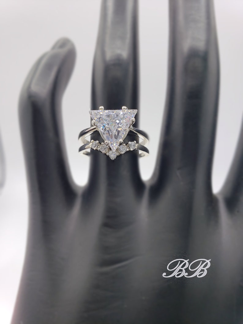 May include: A silver ring with a large triangular-shaped clear stone and a smaller band of stones around the base.