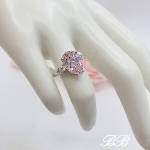 Puede incluir: Un anillo de plata con una piedra preciosa rosa en forma de pera y piedras preciosas m&aacute;s peque&ntilde;as transparentes en la banda.