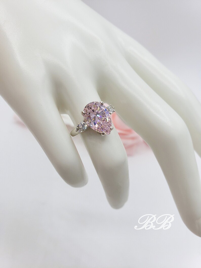 Puede incluir: Un anillo de plata con una piedra preciosa rosa en forma de pera y piedras preciosas m&aacute;s peque&ntilde;as transparentes en la banda.