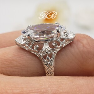 Puede incluir: Un anillo de plata con una gran piedra ovalada transparente engastada en un dise&ntilde;o de filigrana.