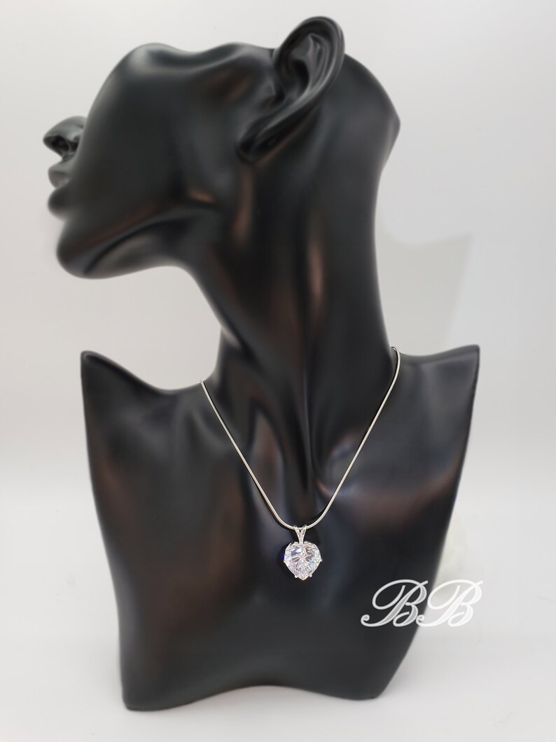 May include: A silver chain necklace with a large, clear heart-shaped pendant. The pendant is made of cubic zirconia stones.