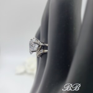 May include: A silver ring with a large, clear, heart-shaped cubic zirconia stone. The ring has smaller cubic zirconia stones on the band.