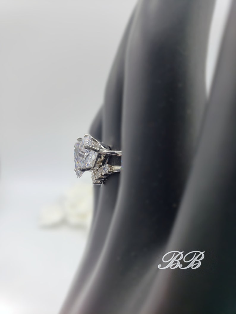 May include: A silver ring with a large, clear, heart-shaped cubic zirconia stone. The ring has smaller cubic zirconia stones on the band.