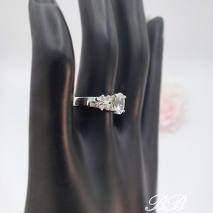 May include: A silver ring with a large oval-shaped clear stone and smaller clear stones on the band.