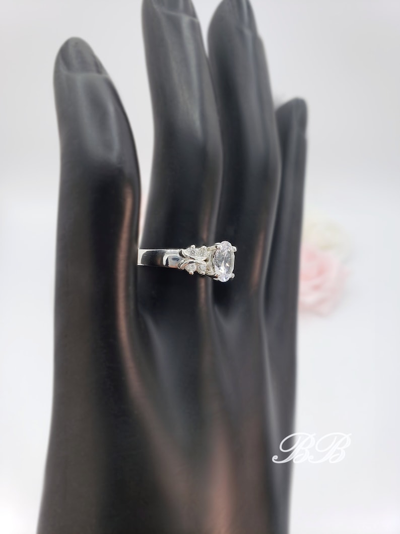 May include: A silver ring with a large oval-shaped clear stone and smaller clear stones on the band.