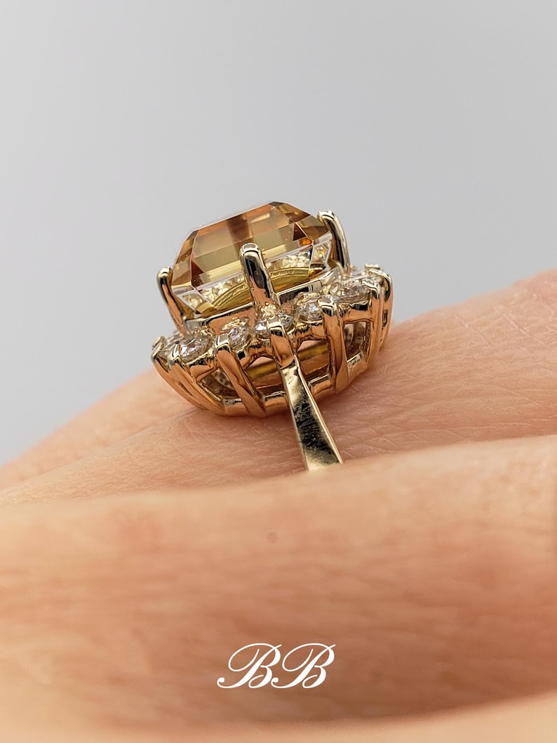 Pode incluir: Um anel de ouro com uma grande gema marrom facetada cercada por um halo de gemas menores e transparentes.