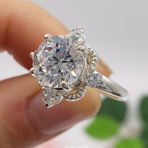 Puede incluir: Un anillo de plata con una gran piedra redonda de circonita c&uacute;bica transparente rodeada de piedras de circonita c&uacute;bica m&aacute;s peque&ntilde;as. El anillo tiene un dise&ntilde;o delicado y adornado.