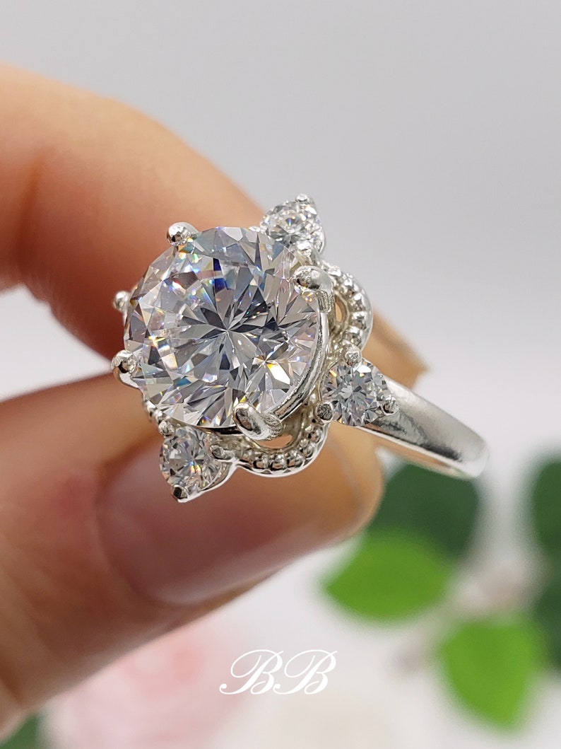 Puede incluir: Un anillo de plata con una gran piedra redonda de circonita c&uacute;bica transparente rodeada de piedras de circonita c&uacute;bica m&aacute;s peque&ntilde;as. El anillo tiene un dise&ntilde;o delicado y adornado.