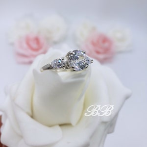 May include: A silver ring with three clear cubic zirconia stones. The center stone is round and the two side stones are pear-shaped.